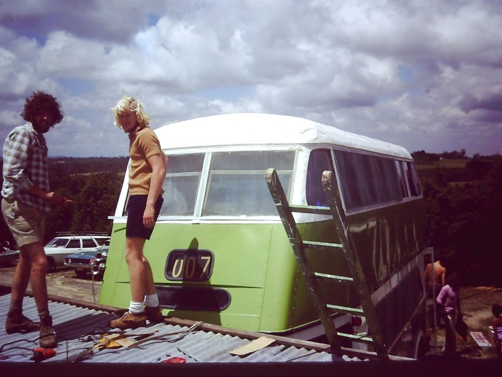 Two young men on the roof of a half-restored green and white double-decker bus